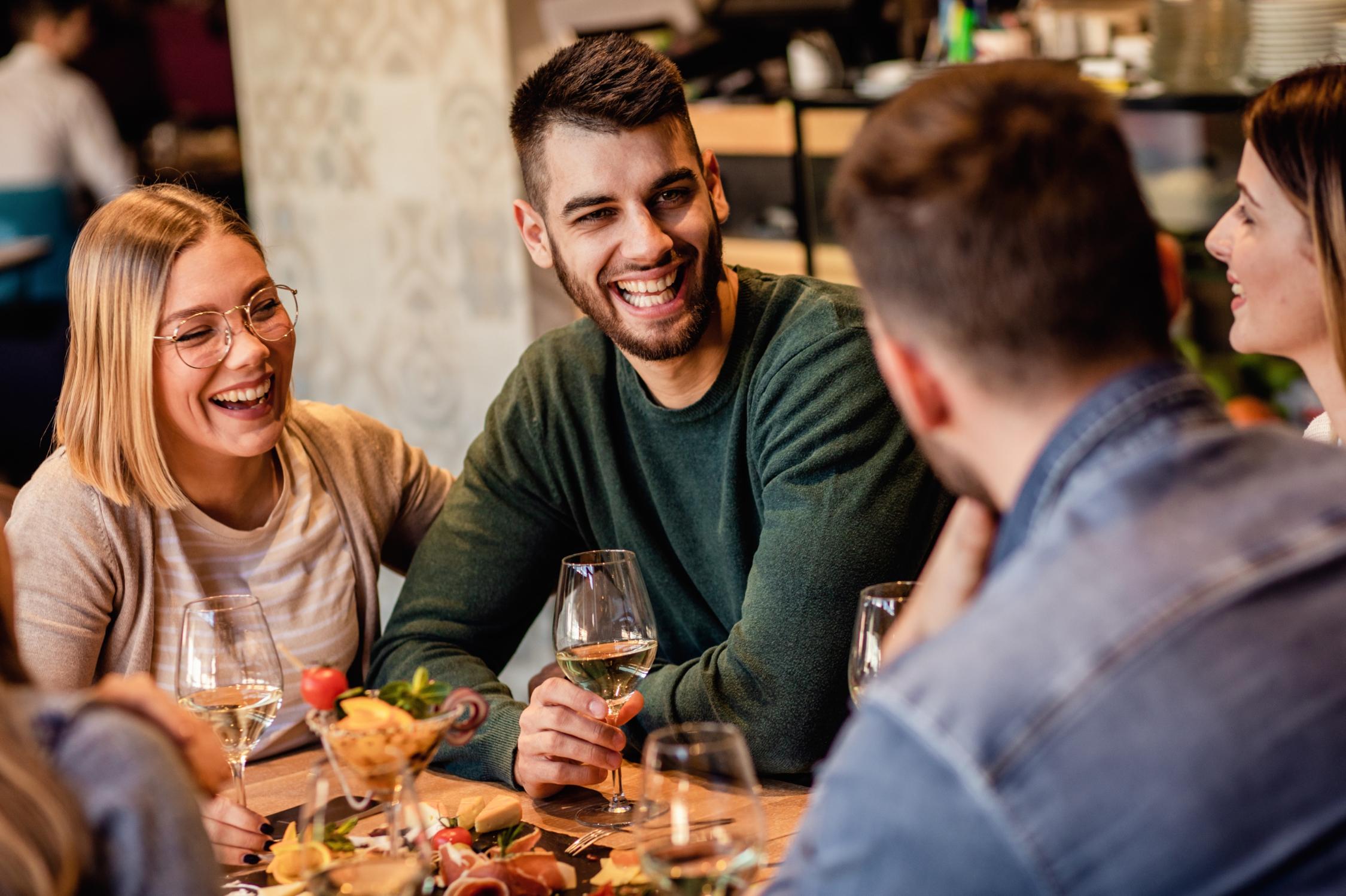 Junge Leute, die sich mit Freude bei einem Glas Wein und Imbiss unterhalten