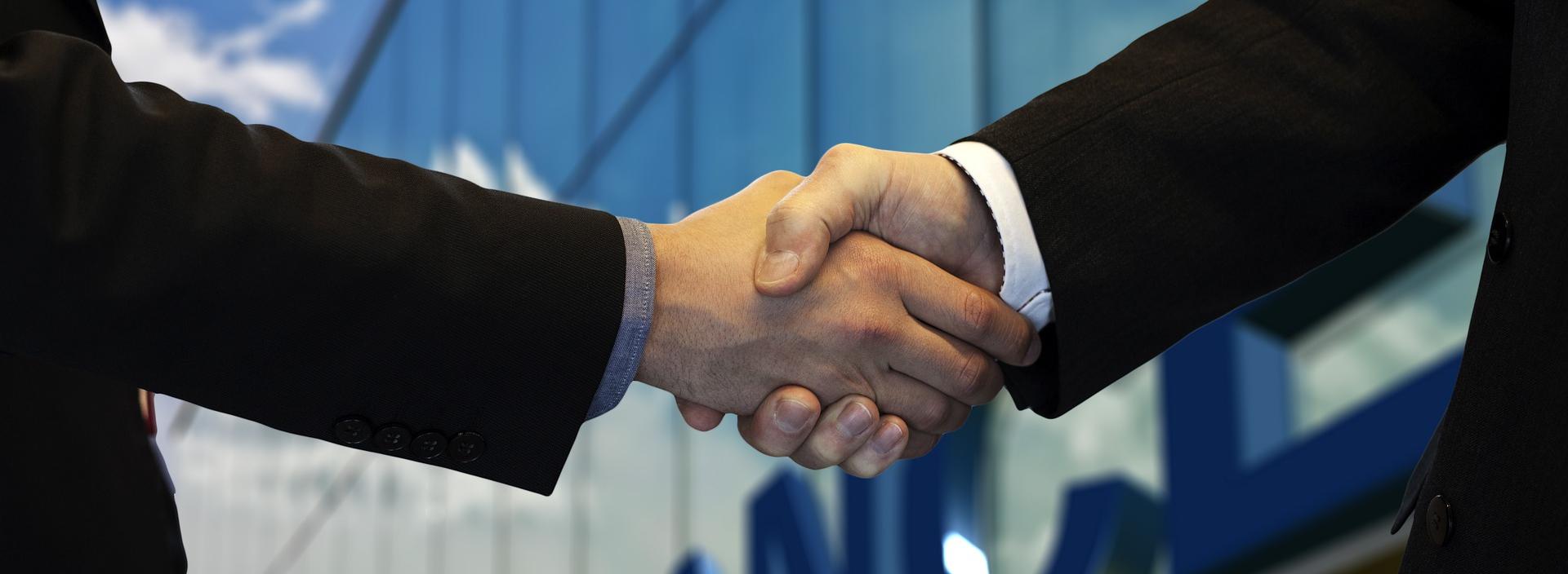2 Personen reichen sich wie zum Vertragsabschluß vor einem Finanzgebäude die Hände
