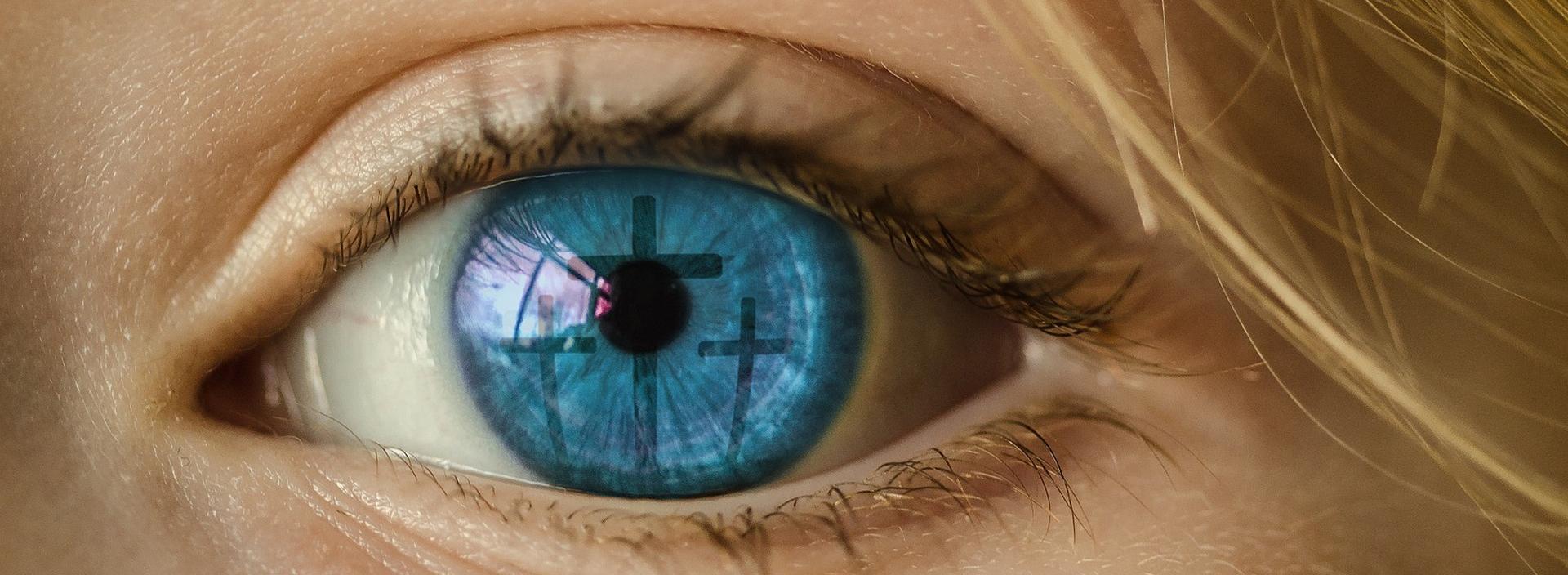 Blaues Auge, in dem sich ein Kreuz spiegelt