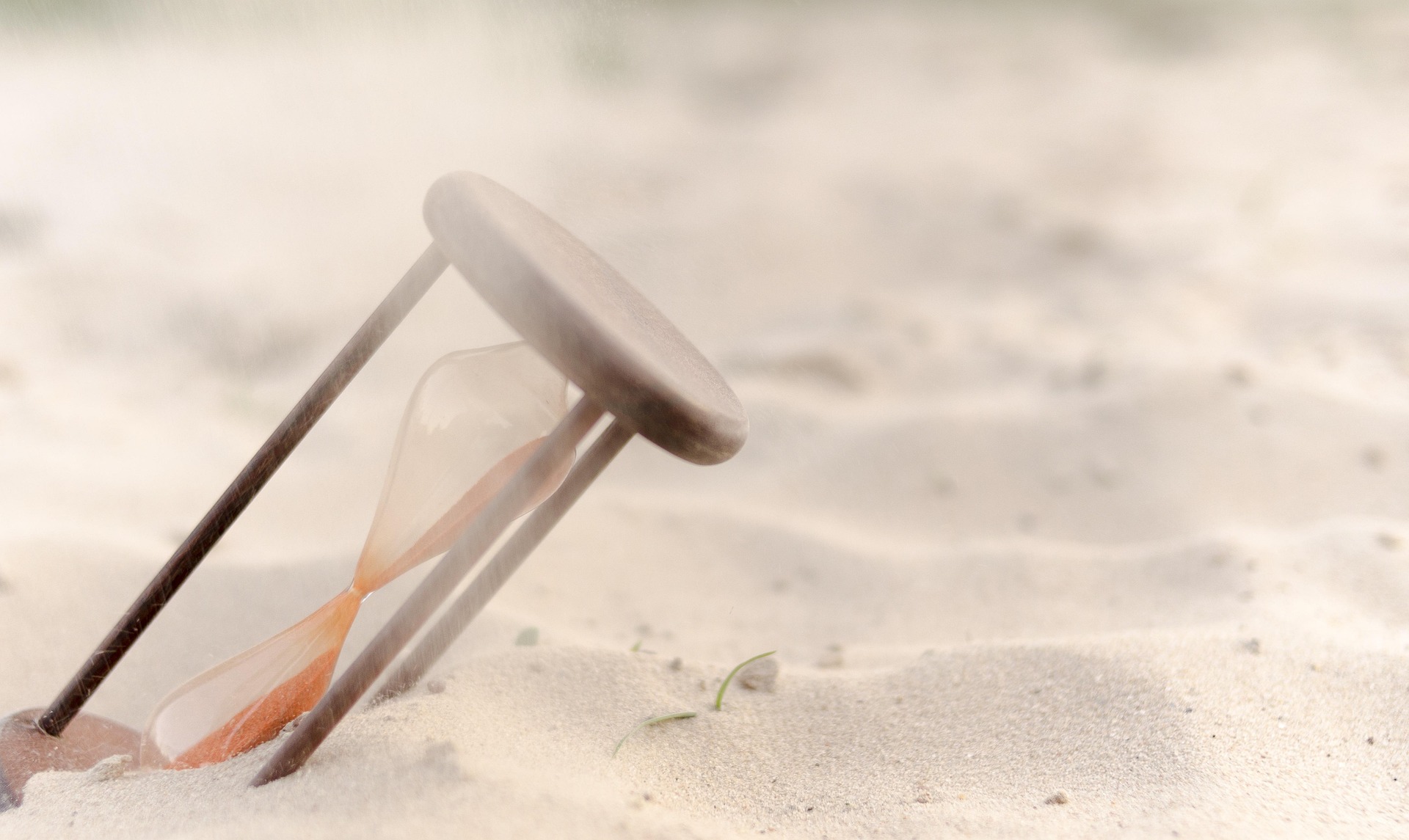 Sanduhr, die schräg im Sand steckt, was den Fluss des Sandes verlangsamt